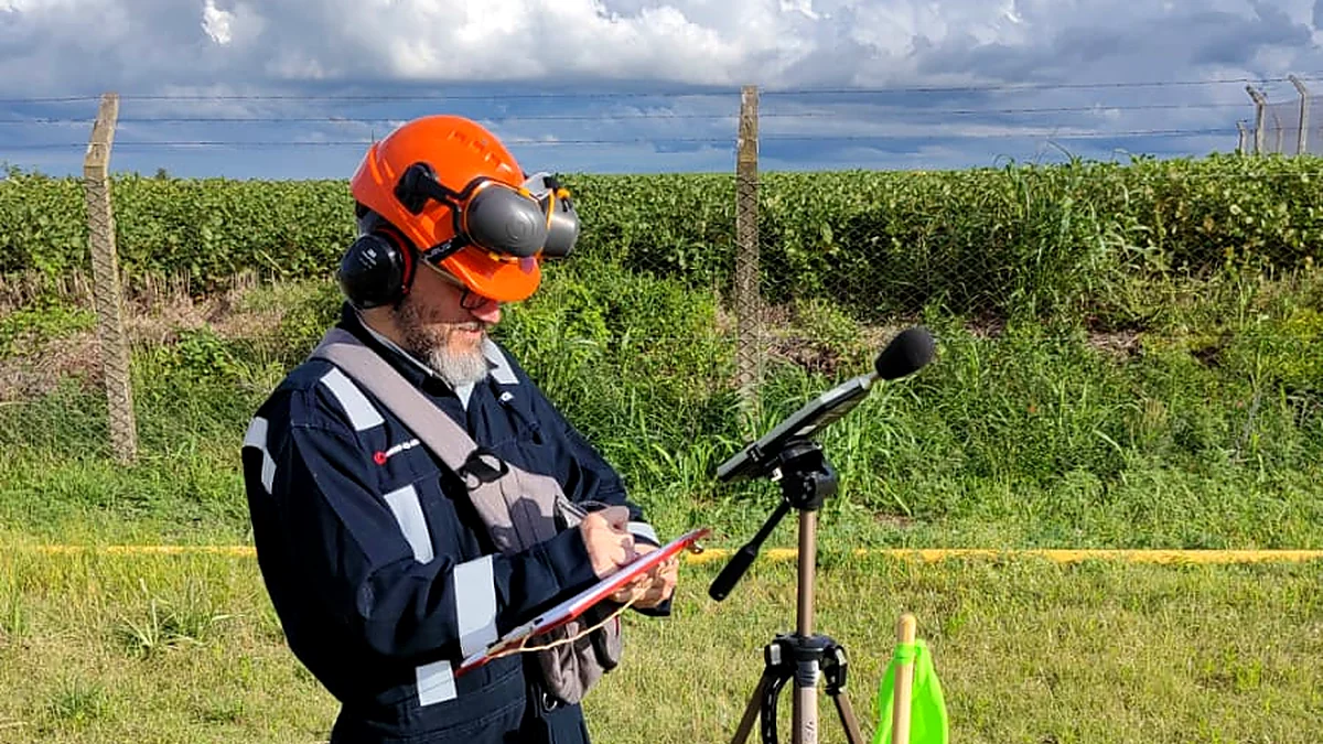 Técnico de Control de Ruido midiendo ruido ambiental con un sonómetro sobre trípode junto a un campo