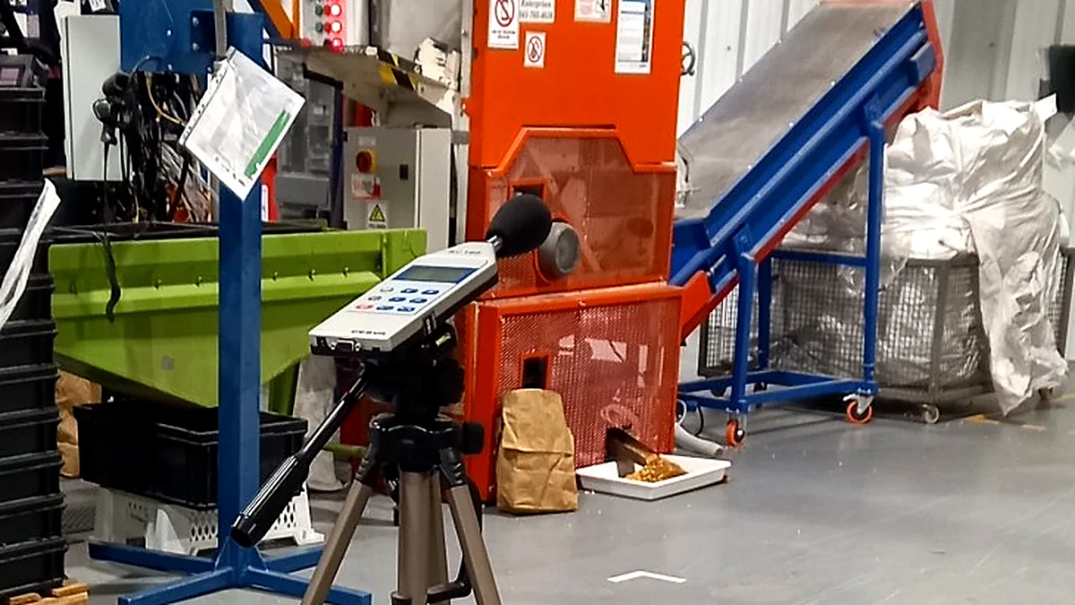 Sonómetro sobre trípode midiendo el ruido de una línea de producción en una planta industrial